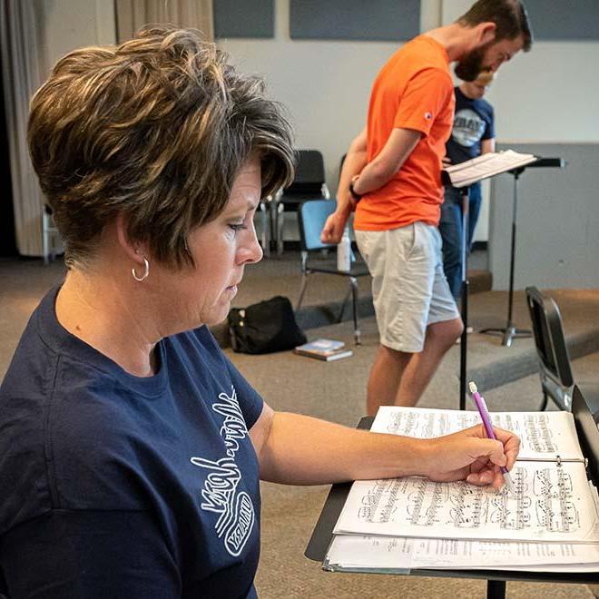 成人音乐学生在乐谱上做笔记，背景是两个学生