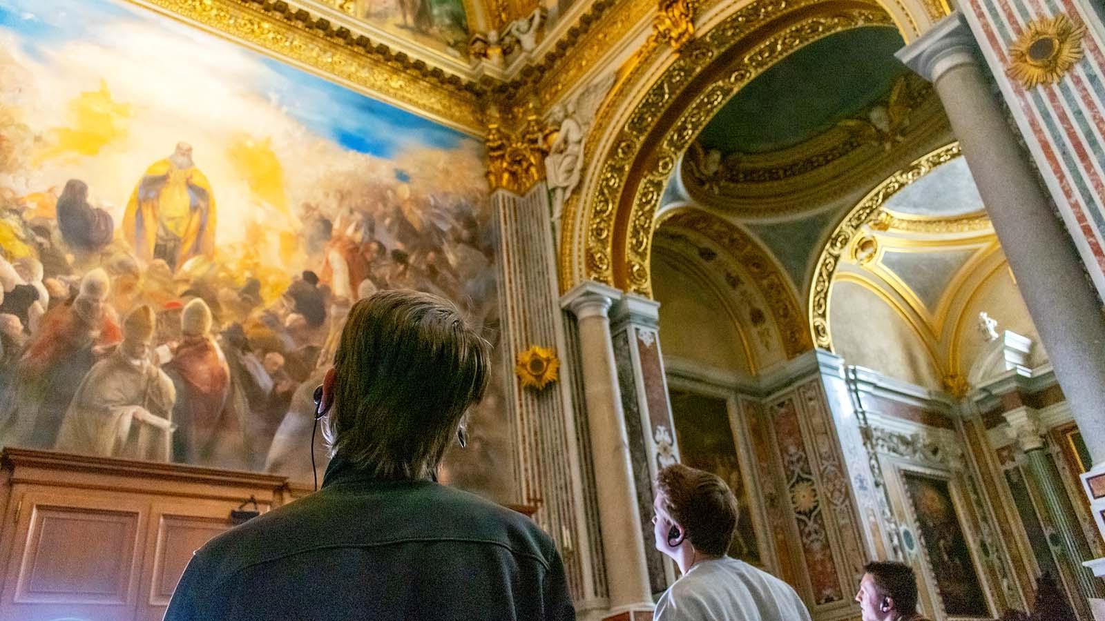三个在罗马留学的学生一边在博物馆欣赏一幅古典绘画，一边听着耳机上的评论